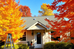 Cozy suburban home with colorful autumn trees, clear sky, and seasonal tools like ladder, gloves, and checklist on porch table.