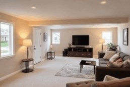 Cozy, modern basement living area with warm lighting and stylish furniture, set in a suburban neighborhood under a clear sky during remodeling.